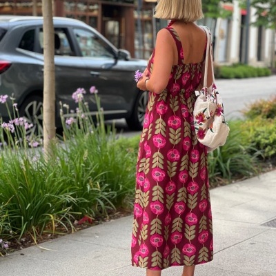 Mulher vista de costas com vestido floral, sapatilhas rosas e bolsa bordada a pé numa calçada urbana
