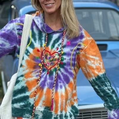 Sweatshirt tie-dye colorida com bordado de coração e cordões trançados, pessoa ao ar livre junto a carro azul