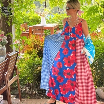 Mulher com vestido longo colorido em ambiente de jardim com mesas e cadeiras de madeira