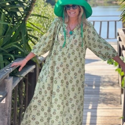 Vestido longo floral verde com chapéu verde em passadeira de madeira perto da água