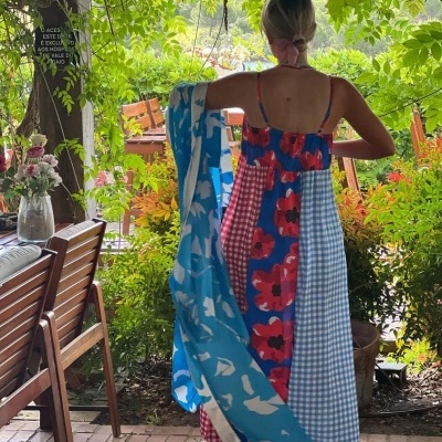 Vestido longo colorido com vários padrões e alças finas, usado por mulher em ambiente com plantas