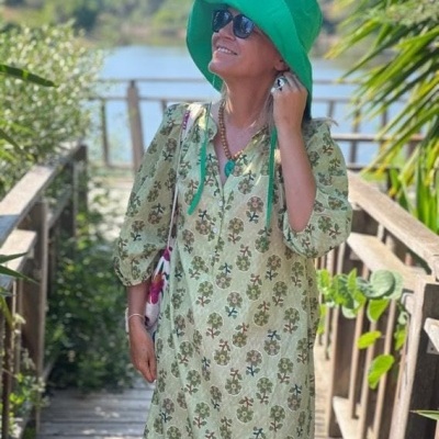 Mulher com vestido floral verde e chapéu verde num passadiço de madeira ao ar livre