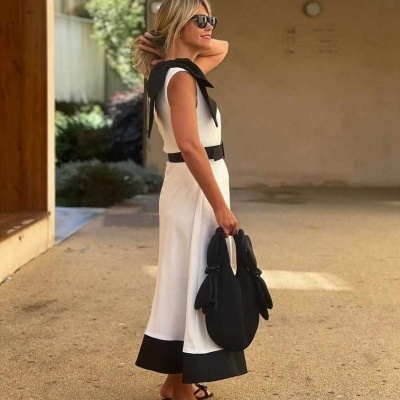 Mulher com vestido midi branco e preto e acessórios pretos num ambiente exterior.