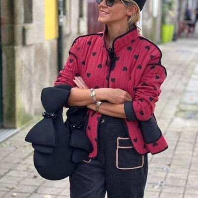 Mulher com casaco vermelho e padrão de corações pretos e acessórios pretos numa rua