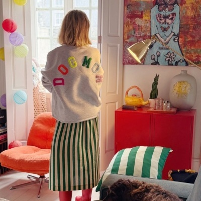 Pessoa de costas com casaco cinza e saia riscada em sala decorada com móvel vermelho e cão no sofá