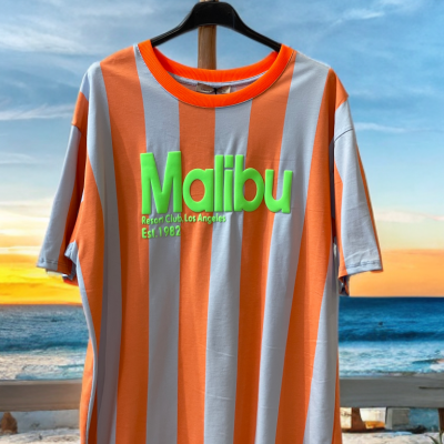 T-shirt riscas laranja e branco com texto verde Malibu pendurada na praia ao pôr do sol