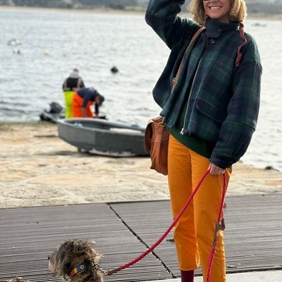 Mulher com casaco xadrez e calças amarelas segura trela de cão perto de cais