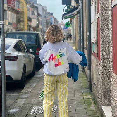 Pessoa de costas com camisola Après ski e calças amarelas com riscas a andar na rua