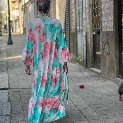 Mulher de costas a usar vestido floral longo com mala azul e scrunchie rosa na rua