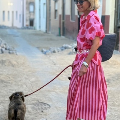 Mulher com camisa rosa de corações vermelhos e saia rosa riscada vermelha a passear cão