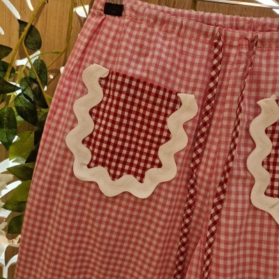 Calça rosa com bolsos vermelhos xadrez decorados com borda branca ondulada.