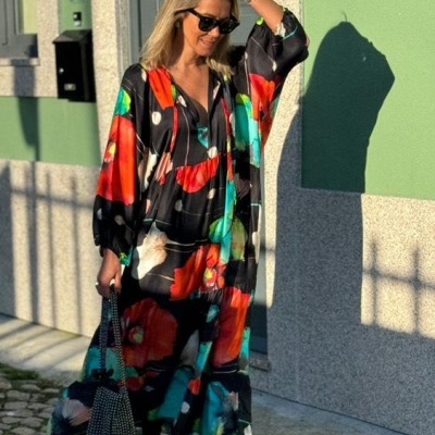 Vestido comprido fluído com padrão floral colorido e fundo preto sob luz solar