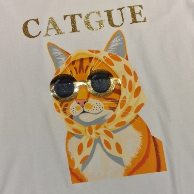 T-shirt branca com estampa de gato laranja de óculos e lenço, texto dourado CATGUE