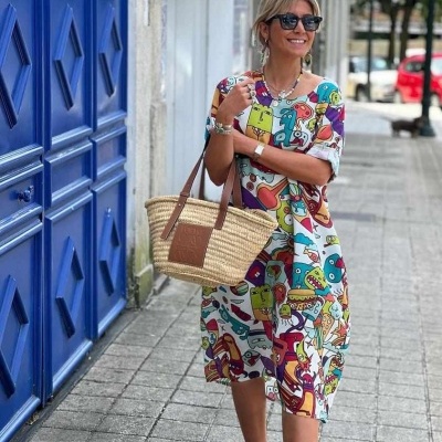 Mulher com vestido midi colorido e mala de palha em rua urbana