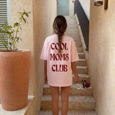 Pessoa com camisola rosa claro com texto COOL MOMS CLUB vista de costas num corredor estreito com escadas de pedra