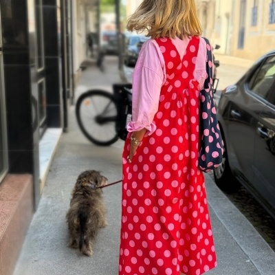 Vestido vermelho com bolinhas rosa usado sobre camisa rosa com saco azul às bolinhas.