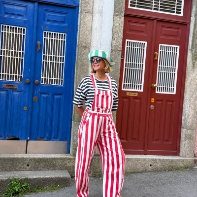 Mulher com roupa riscada vermelha, branca e preta em rua com portas coloridas ao fundo