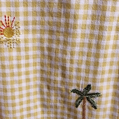 Tecido xadrez amarelo com bordados coloridos de flores, palmeira e ananás.