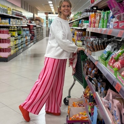 Mulher de calças rosas às riscas vermelhas e camisola branca a fazer compras num supermercado.