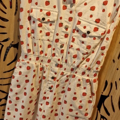 Vestido branco com padrão de morangos vermelhos em cabide de madeira