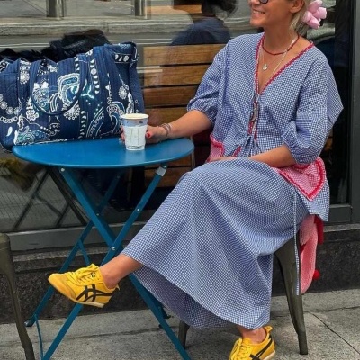 Mulher com vestido azul e ténis amarelos numa esplanada com bolsa azul e mesa azul
