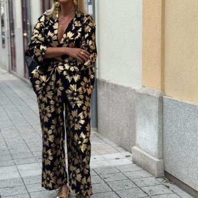 Mulher com conjunto floral dourado e preto, sapatos dourados e óculos escuros em passeio urbano