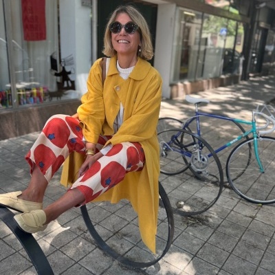 Mulher sentada em suporte metálico circular na rua com casaco amarelo e calças estampadas
