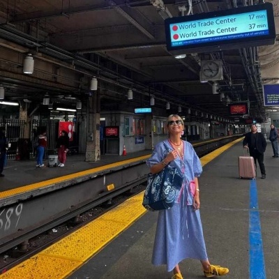 Mulher em plataforma de comboio com vestido azul claro, sapatos amarelos e bolsa azul escura