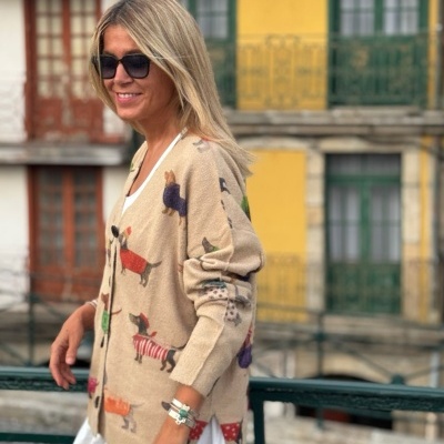 Cardigan bege com padrão de cães coloridos, usado por mulher com vestido branco, em ambiente urbano