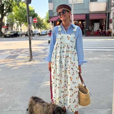 Mulher com vestido branco estampado e cão castanho numa rua urbana