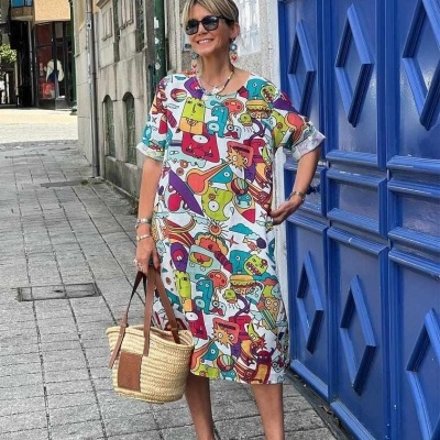 Mulher vestindo vestido colorido abstrato, segurando mala de palha e usando sapatos azuis, em rua com porta azul