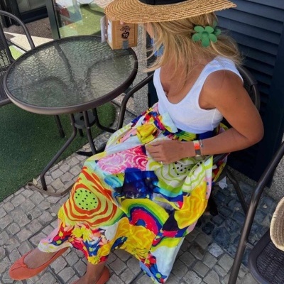 Mulher a usar saia colorida, top branco e chapéu de palha sentada ao ar livre
