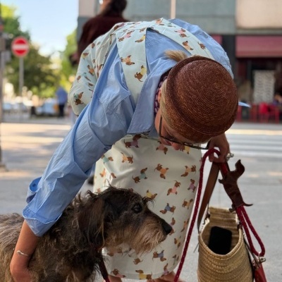 Pessoa a acariciar cão com avental de padrão de cães e segurando trela vermelha e bolsa de palha