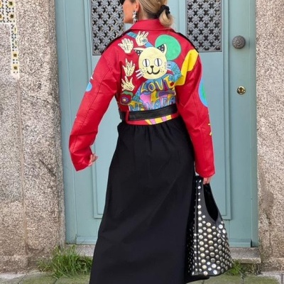 Casaco vermelho em pele com padrão colorido de gato e a palavra LOVE, saia preta, sapatos e mala com tachas prateadas