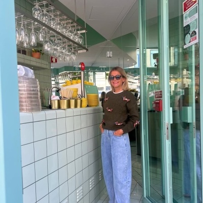 Café moderno com balcão azulejado, copos pendurados e mulher vestindo camisola e calças largas.