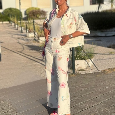 Mulher com conjunto branco estampado e óculos de sol a sorrir ao ar livre