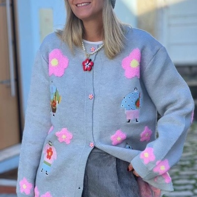 Cardigan cinzento com flores cor-de-rosa e detalhes coloridos usado por mulher com gorro cinzento e óculos escuros