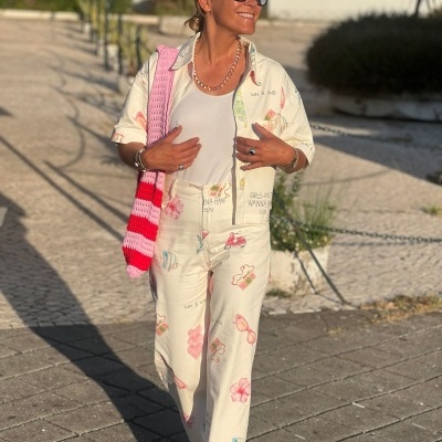 Mulher com conjunto claro estampado, top branco, bolsa rosa às riscas e óculos escuros
