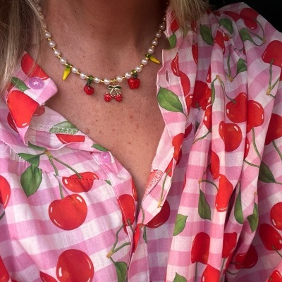 Camisa rosa com cerejas vermelhas e colar com pendentes de frutas.