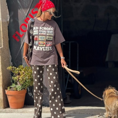 Mulher com camiseta estampada e calças com bolinhas a passear um cão numa rua urbana