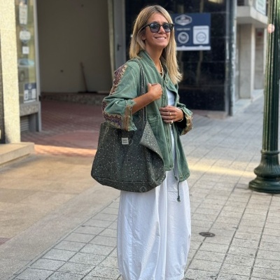 Mulher com casaco verde e calças brancas na rua com bolsa verde escuro e sapatilhas bege.