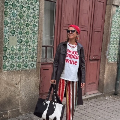 Pessoa com roupas coloridas e casaco de pele frente a porta vermelha e azulejos verdes