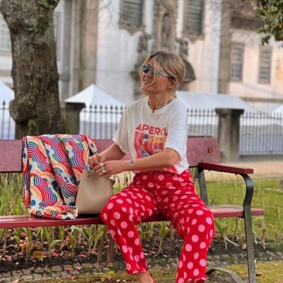 Mulher sentada num banco com roupa colorida e acessórios ao ar livre