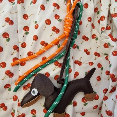 Chaveiro cachorro peluche castanho com corda colorida sobre tecido com padrão de cerejas