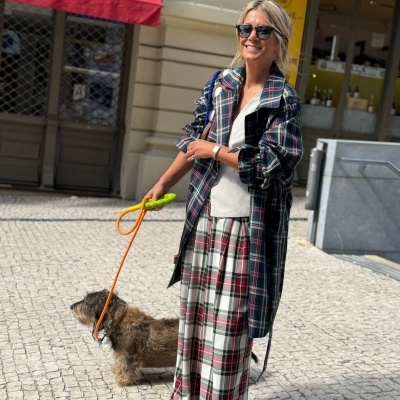 Mulher com vestido e casaco xadrez a passear cão numa calçada portuguesa