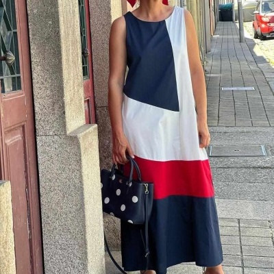 Mulher com vestido longo colorido, sapatos vermelhos e bolsa preta com bolinhas brancas em rua urbana