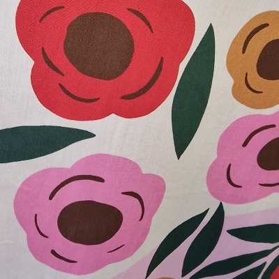 Tecido com padrão floral colorido composto por flores vermelhas, rosas e amarelas com folhas verdes.