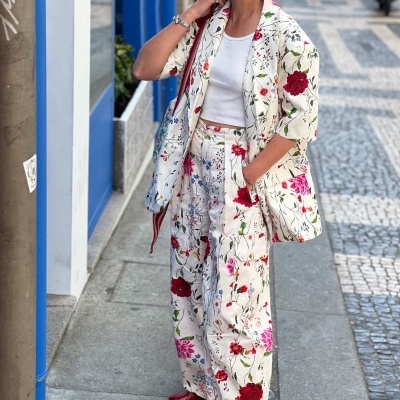 Conjunto branco com flores coloridas, casaco 3/4 e calças largas, top branco, sapatos vermelhos.