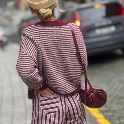 Pessoa com chapéu de palha, camisola às riscas vermelhas e brancas e calças às riscas roxas com bolsos de coração