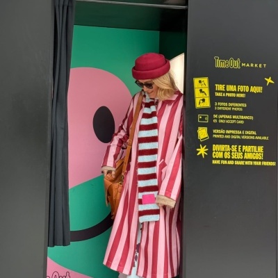 Mulher dentro de cabine fotográfica preta com letreiro Photobooth em neon vermelho